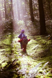 2 Kinder stapfen im Sonnenstrahl durch den Wald