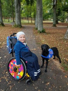 Nora (ein Mädchen im Rollstuhl) und Zoe (ein Assistenzhund)