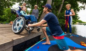Junge im Rollstuhl wird auf ein Stand-Up_paddling Board gehoben