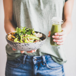 Person hält eine Schale mit grünem Gemüse in der einen und einen grünen Smoothie in der anderen Hand