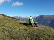 ältere Person auf Bank vor Alpenpanorama