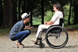 Frau hockt vor Frau im Rollstuhl