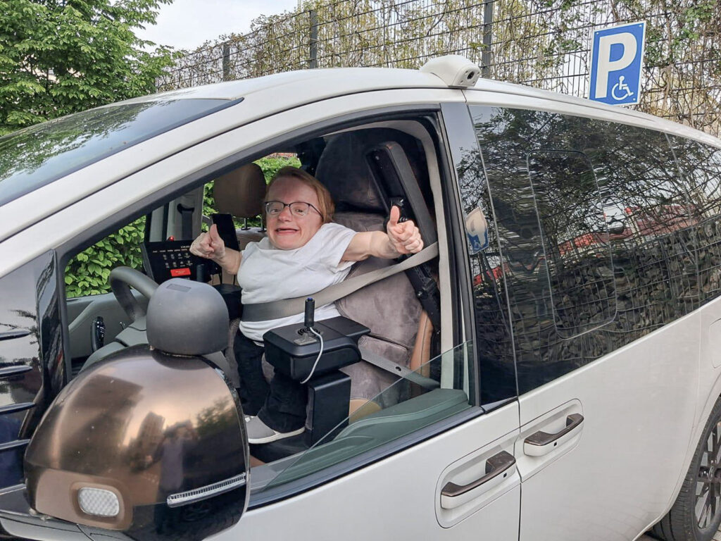 Marina sitzt in ihrem individuell angepassten Paravan Hyundai Staria und zeigt beide Daumen nach oben.