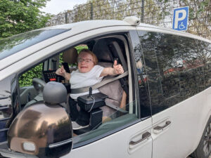 Marina sitzt in ihrem individuell angepassten Paravan Hyundai Staria und zeigt beide Daumen nach oben.