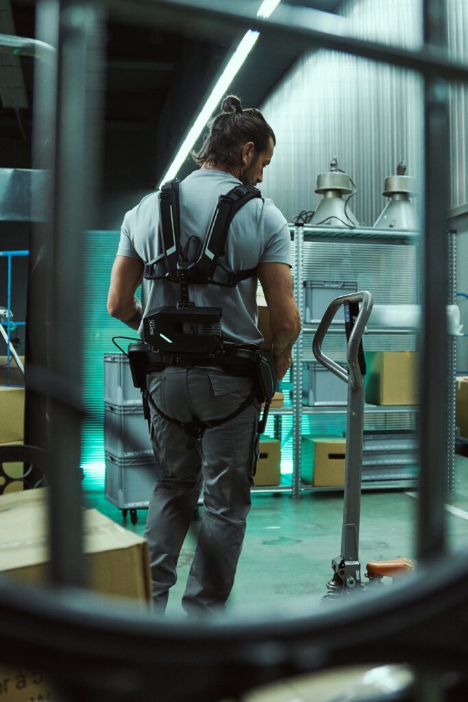 Arbeiter tr&auml;gt ein R&uuml;cken-Exoskelett im Lager.