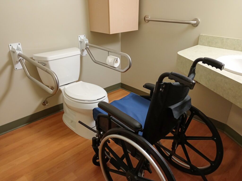Rollstuhl in einem barrierearmen Badezimmer neben Toilette und Haltegriffen