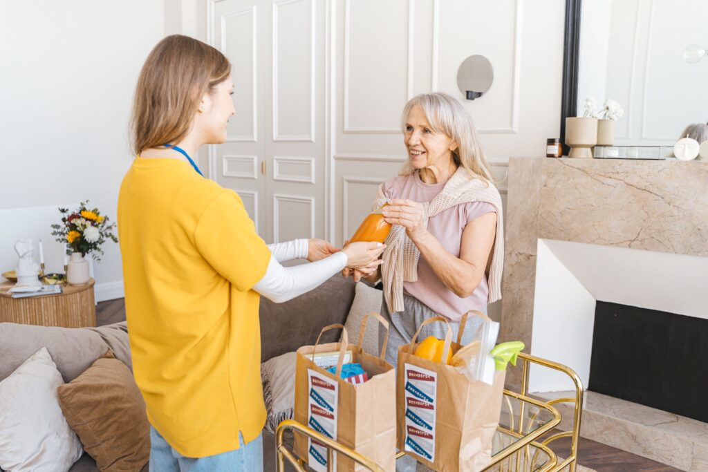 Pflege und Unterstützung im Alltag Betreuungskraft übergibt einer Seniorin Einkäufe